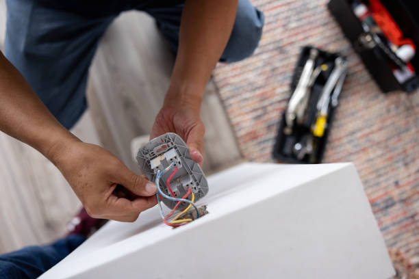 A person's hands hold a disassembled electrical outlet or switch, showing the internal wiring and components, with tools visible on a brick surface in the background.RetryClaude can make mistakes. Please double-check responses.